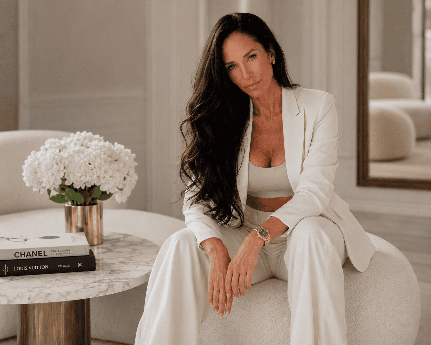 Elegant woman in white suit sitting on a sofa in a luxurious room.