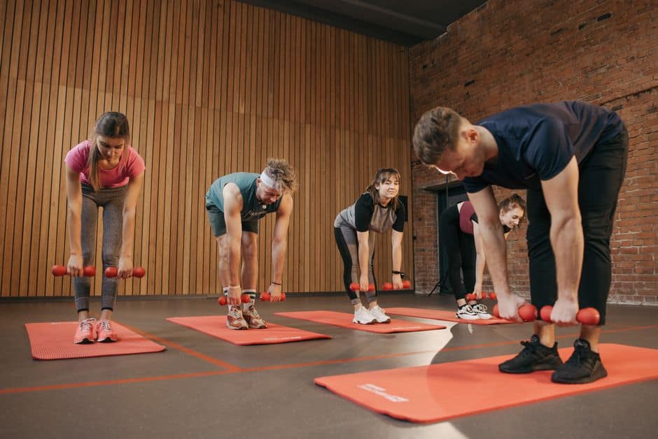 Group of people doing weightlifting exercises in a gym.