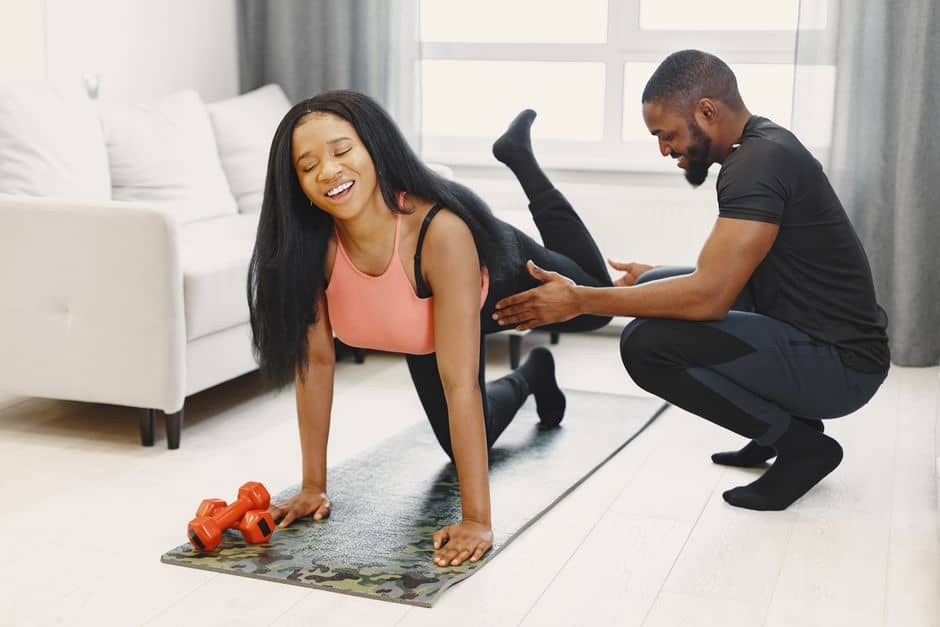 Woman doing push-ups with trainer assisting at home gym.